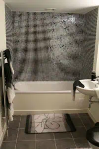 Bathroom with mosaic tile wall and bathtub, featuring a sink and towel rack.