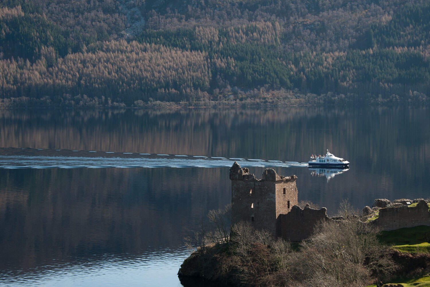 Historic Highland Castle by Loch Ness with boat passing by.