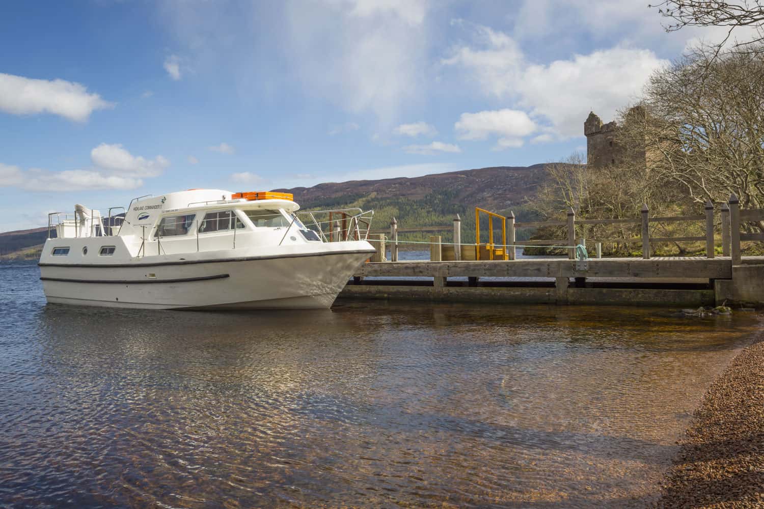 Boat moored at Highland Club Scotland waterfront with scenic mountain backdrop.