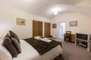 Highland Club Scotland bedroom with comfortable bed, TV, and wooden furniture.
