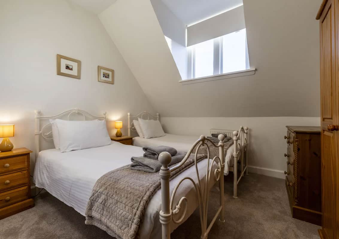 Cozy bedroom featuring twin beds, wooden furniture, and a skylight in a Highland Club Scotland prope.