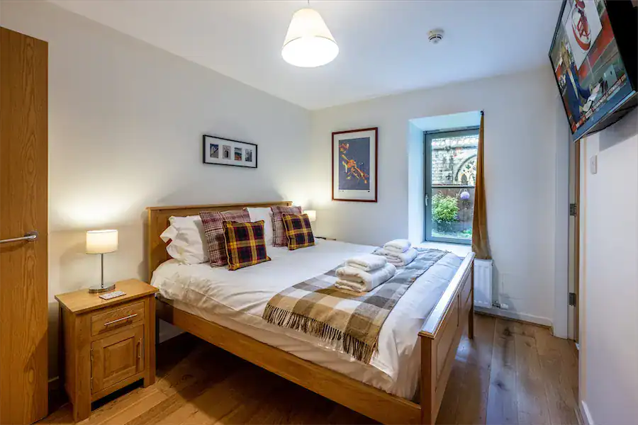 Comfortable bedroom at Highland Club with wooden bed frame, plaid cushions, and natural light from w.