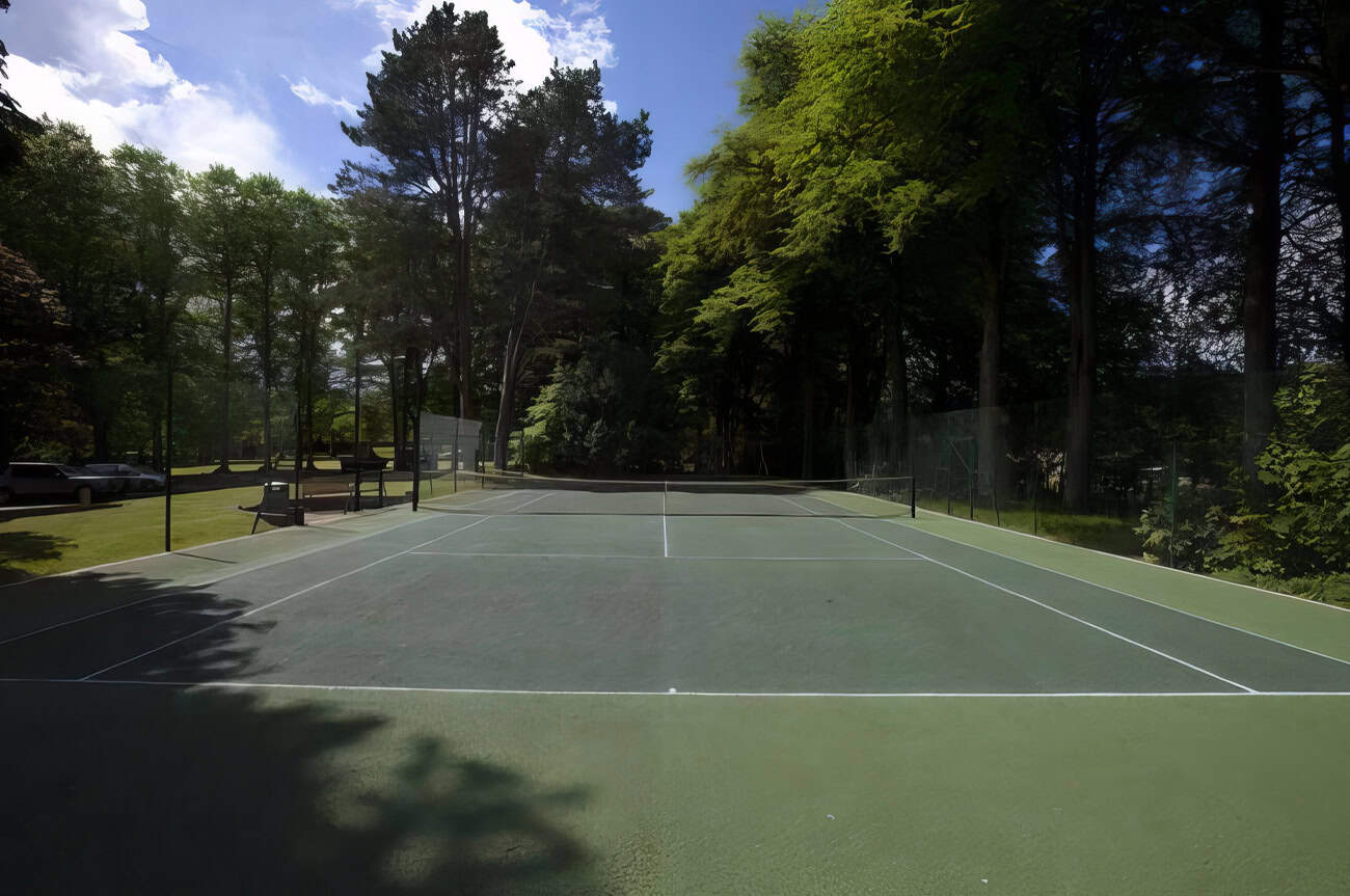 Tennis court facilities at Highland Club Scotland, surrounded by lush trees and natural scenery.
