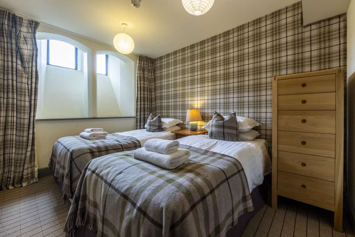 Bright Highland Club bedroom with twin beds and traditional tartan decor.