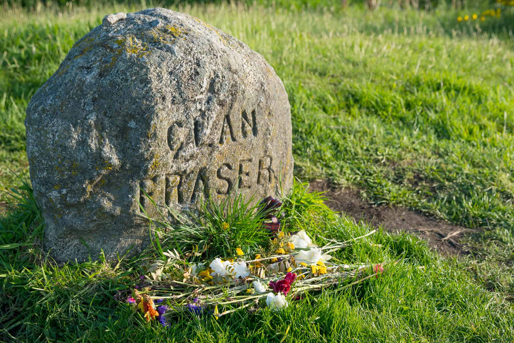 Clachan Traser memorial stone with flowers in a grassy area.