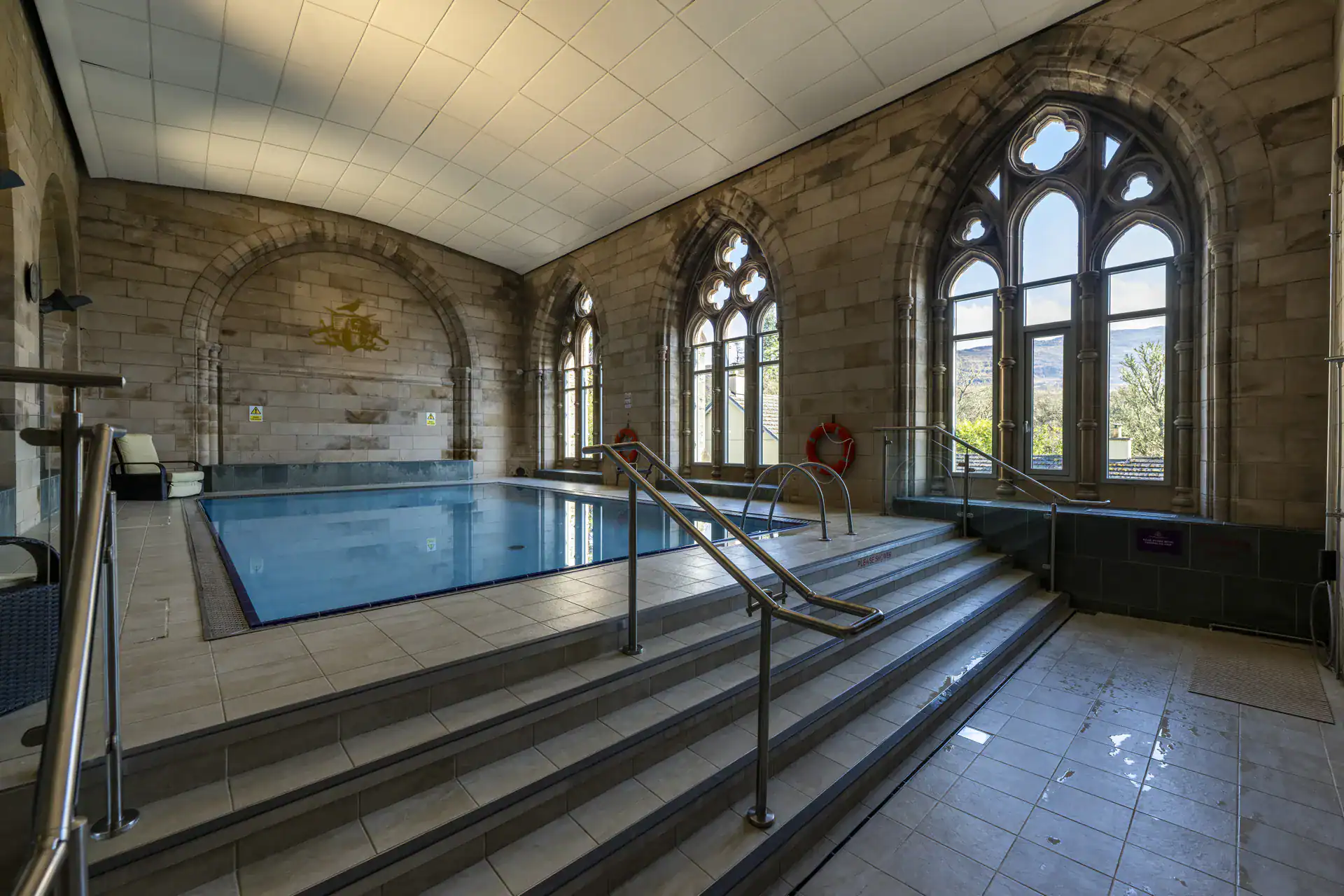 Elegant indoor swimming pool with Gothic windows and stone walls, offering a luxurious relaxation sp.