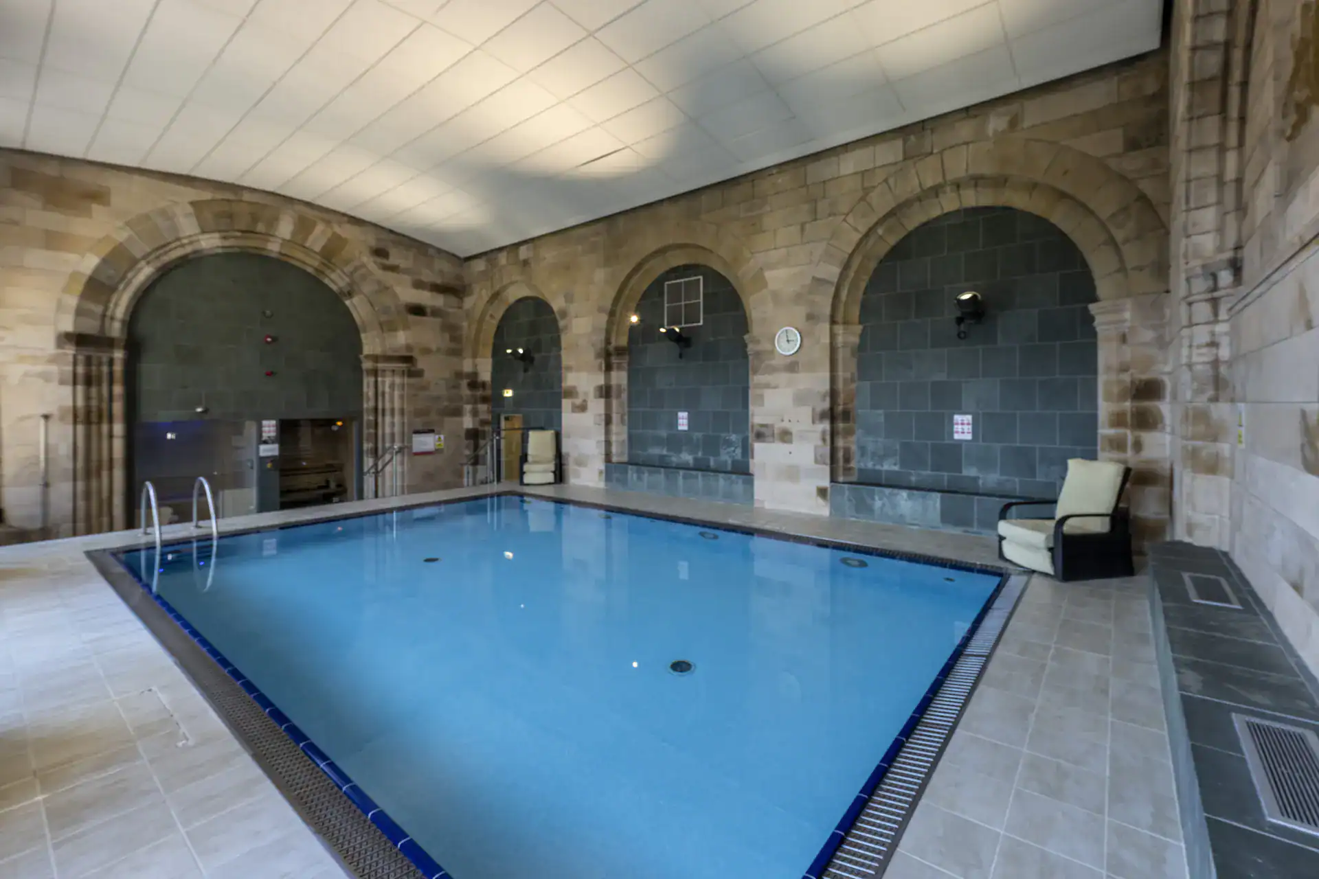 Indoor swimming pool with stone arches and relaxing seating area at Highland Club Scotland.