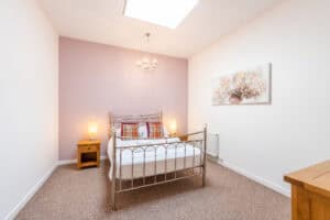Comfortable bedroom with metal bed frame and soft lighting, featuring a pink accent wall and floral.