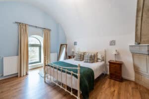 Bedroom with white iron bed, wooden side table, and large arched window.