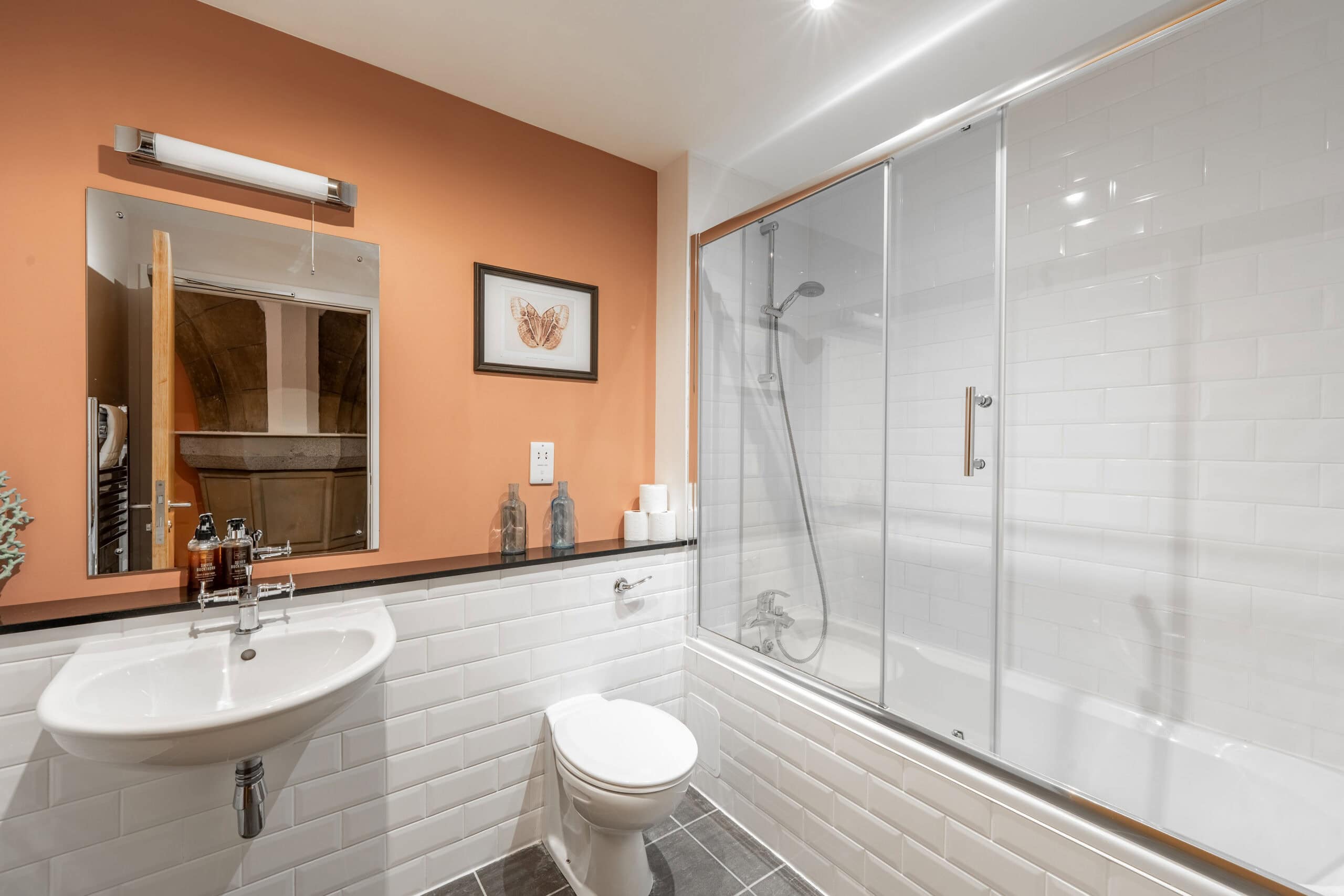 Modern bathroom with glass-enclosed shower and white subway tiles, featuring a sink, toilet, and war.