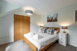 Modern bedroom with wooden bed frame, bedside lamps, and deer artwork at Highland Club Scotland.