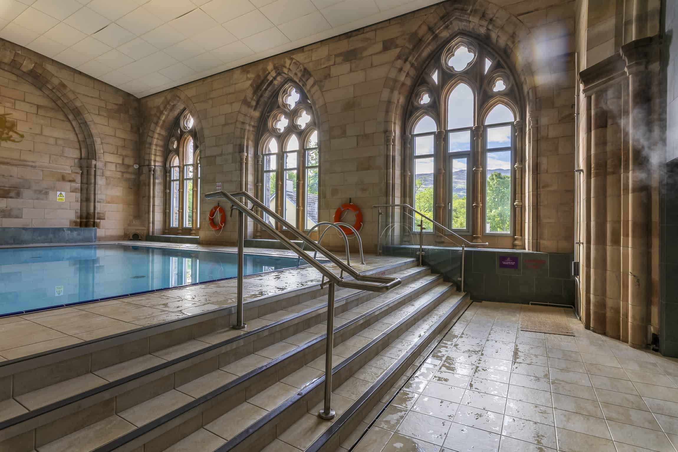 Relaxing indoor swimming pool at Highland Club Scotland with stone architecture and large arched win.