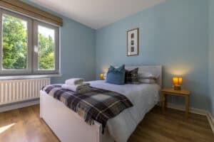 Modern bedroom with blue walls, large window, and cozy bedding in Highland Club Scotland development.
