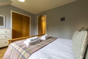 Comfortable bedroom with neatly made bed and wooden furniture at Highland Club Scotland.