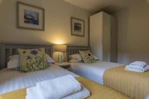 Modern bedroom with twin beds, colourful cushions, and scenic artwork in Highland Club Scotland.