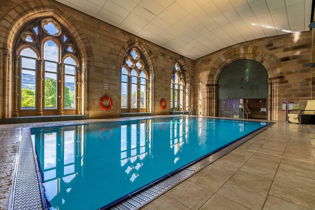 Indoor swimming pool with large arched windows and scenic views at Highland Club Scotland.