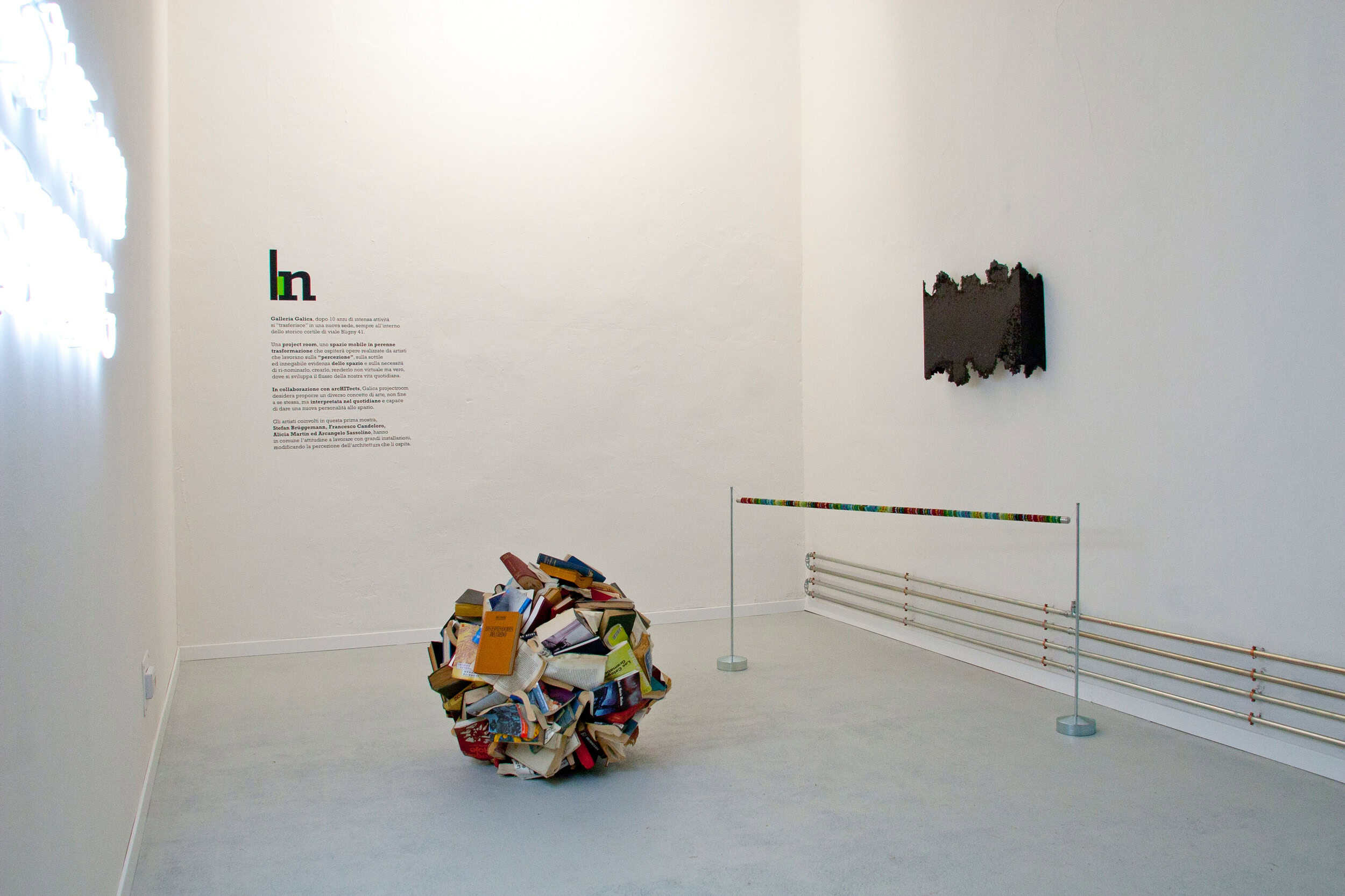 Contemporary Art Installation With A Pile Of Books And Wall Sculptures In A Gallery.