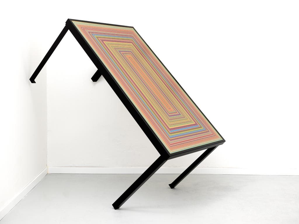 Colorful geometric artwork on a tilted black table in a white room.