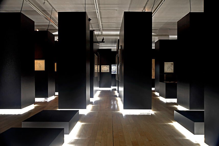 Modern art exhibition with black display panels and illuminated flooring.