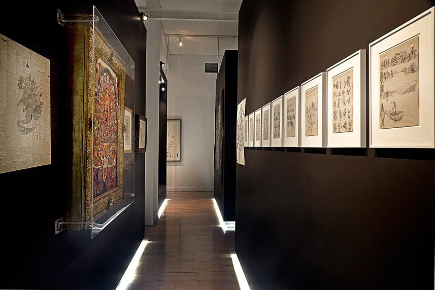 Art gallery interior with framed artworks on dark walls and wooden floor.