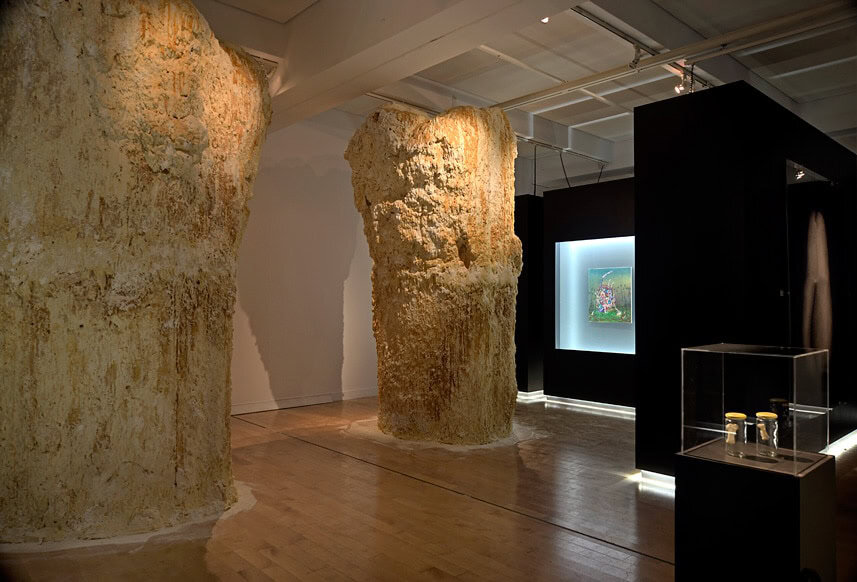 Interior view of an exhibition with large stone-like columns and display cases.