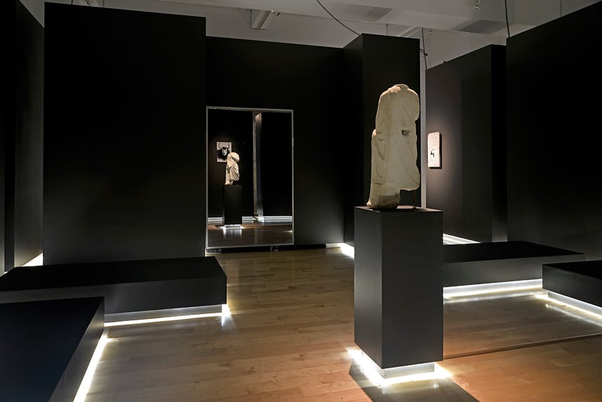 Modern art gallery interior with sculptures and black walls.