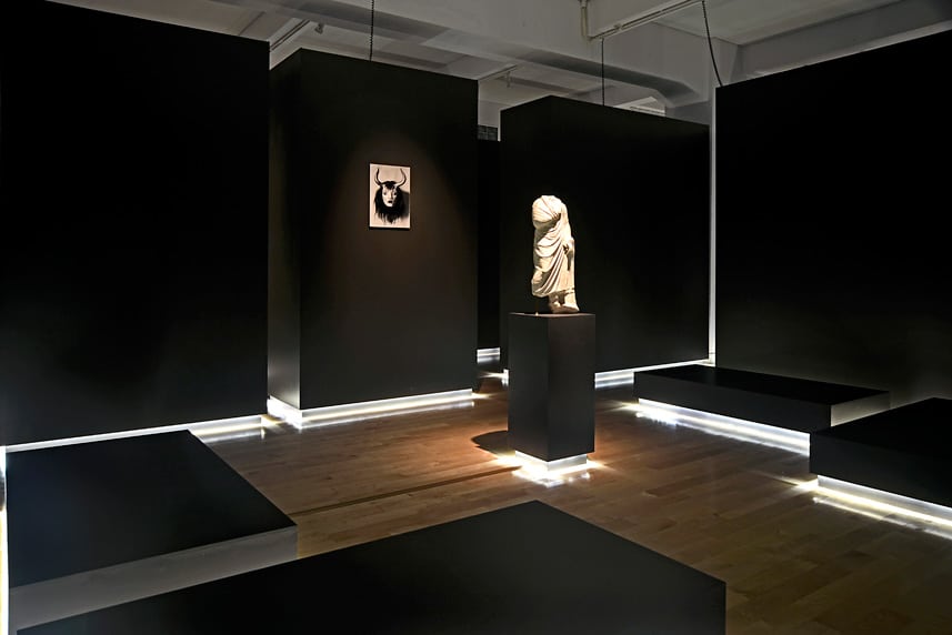 Modern art gallery with black walls and illuminated sculptures and artwork.