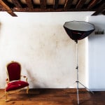 Photography Studio Setup With A Red Velvet Chair And Softbox Light In A Minimalist Room.