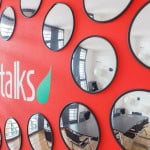 Modern Office Interior With A Red Wall Featuring Multiple Round Mirrors And 'Talks' Logo.