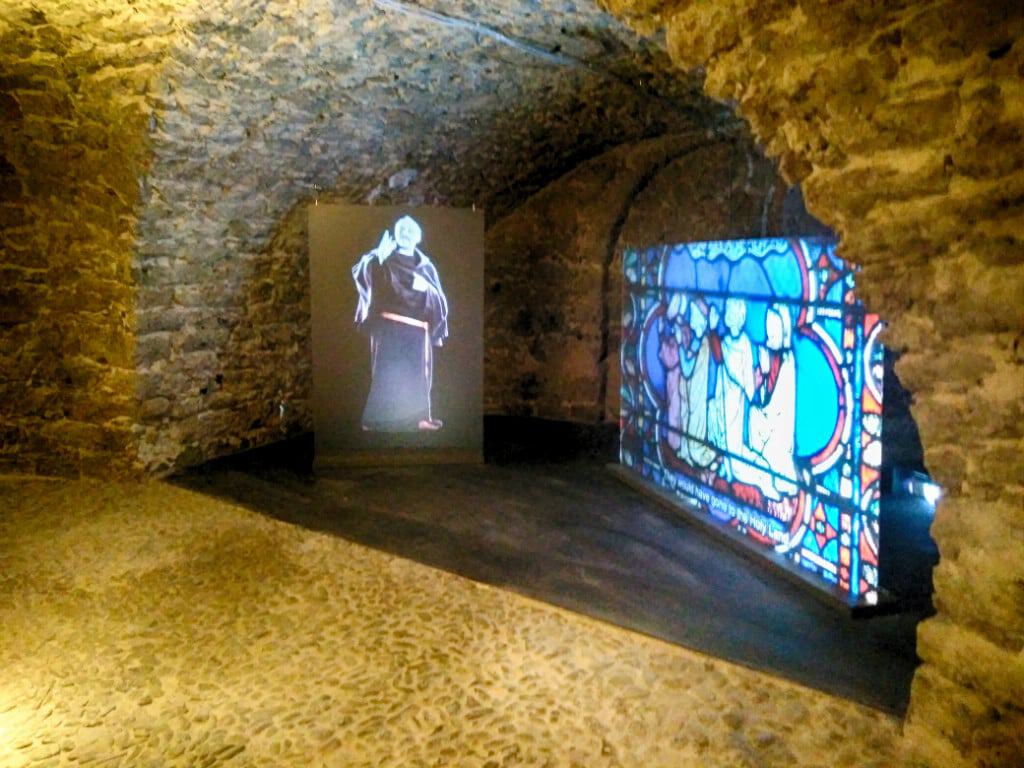 Interior of a historic stone building with stained glass window and statue display.