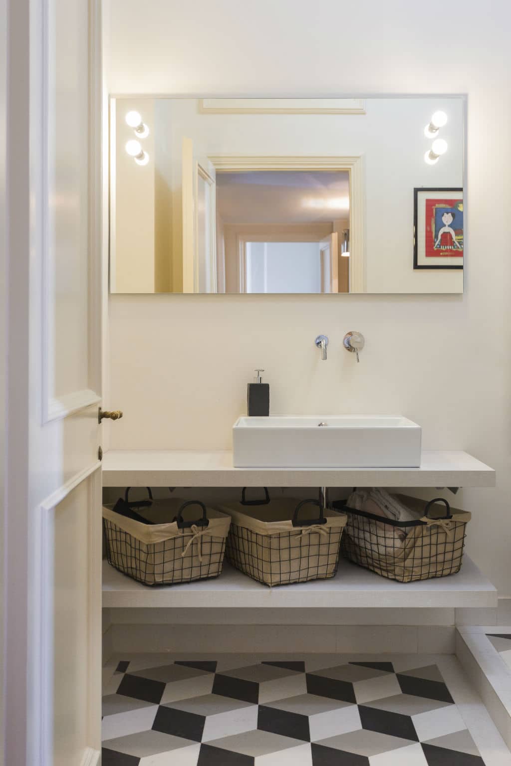 Modern bathroom with white sink, large mirror, and geometric floor tiles.