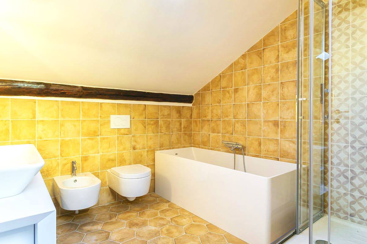 Modern bathroom with beige tiles, bathtub, bidet, and shower enclosure.