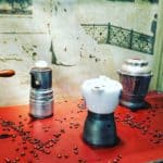 Old-Fashioned Coffee Machines On A Red Table With Coffee Beans Scattered Around.