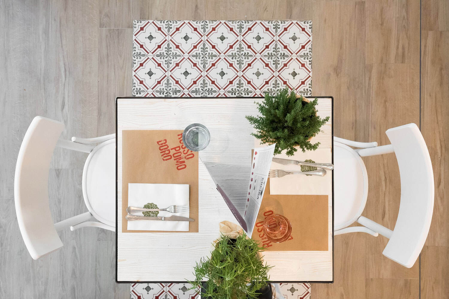 Top view of a restaurant table set for two with plants and menus.