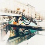 Colorful Graffiti On Urban Bridge Over Water In Foggy Cityscape.