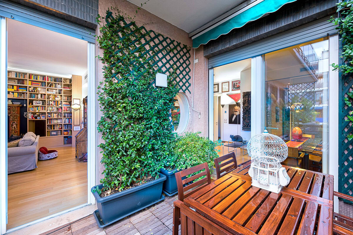 Modern balcony with wooden table, chairs, and lush greenery in an urban apartment.
