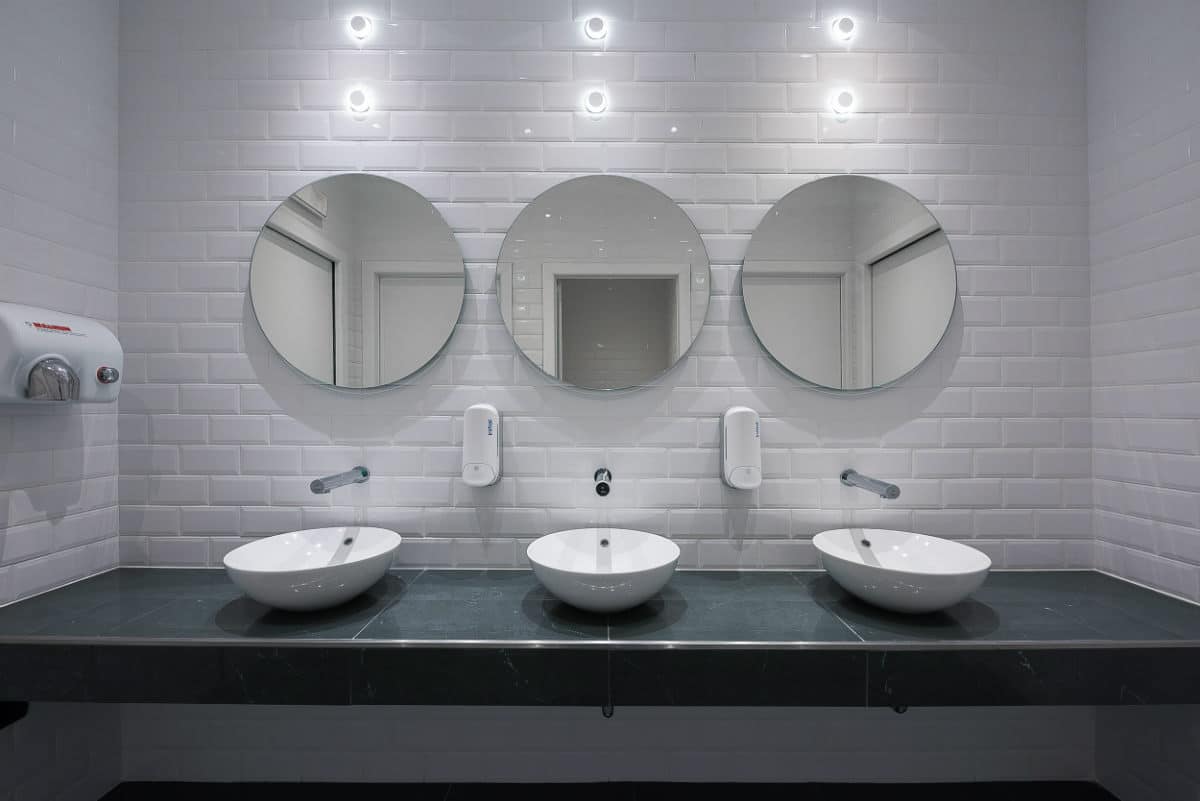 Modern public restroom with three round mirrors and white brick wall.