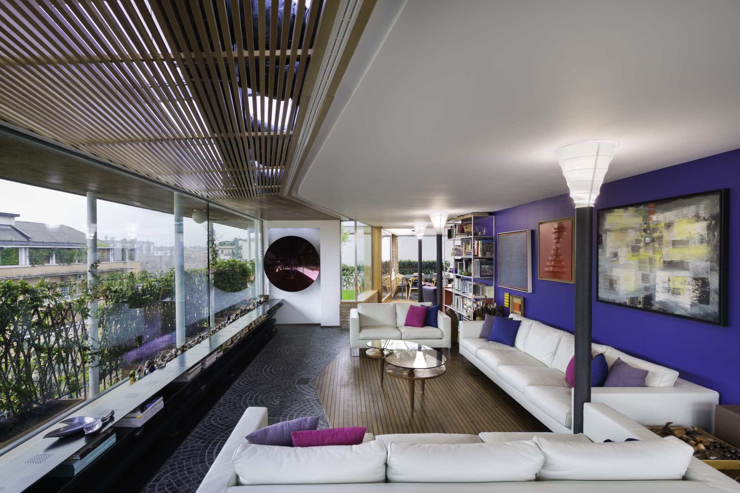 Modern living room with large windows, white sofas, and vibrant purple walls.