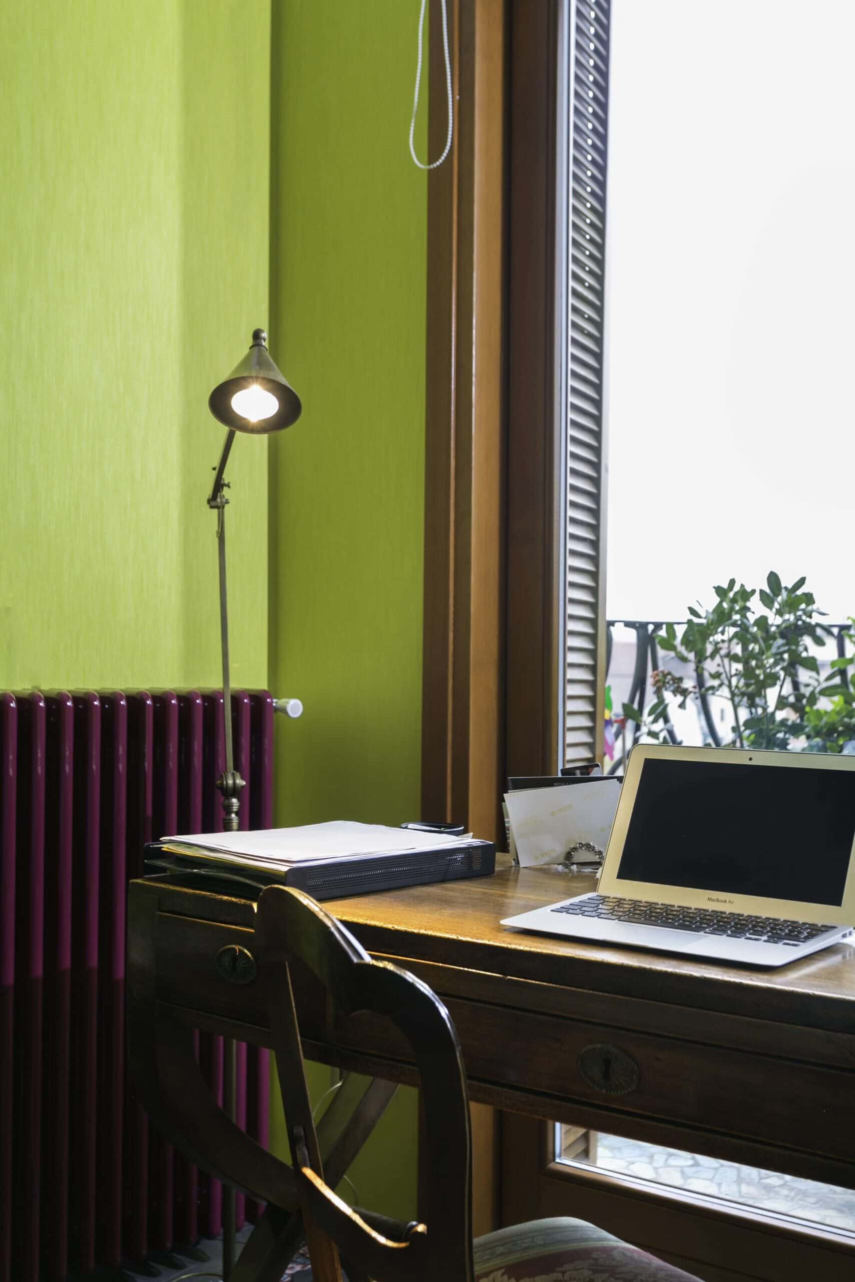 Cozy workspace with green wall, desk, laptop, and natural light from window.
