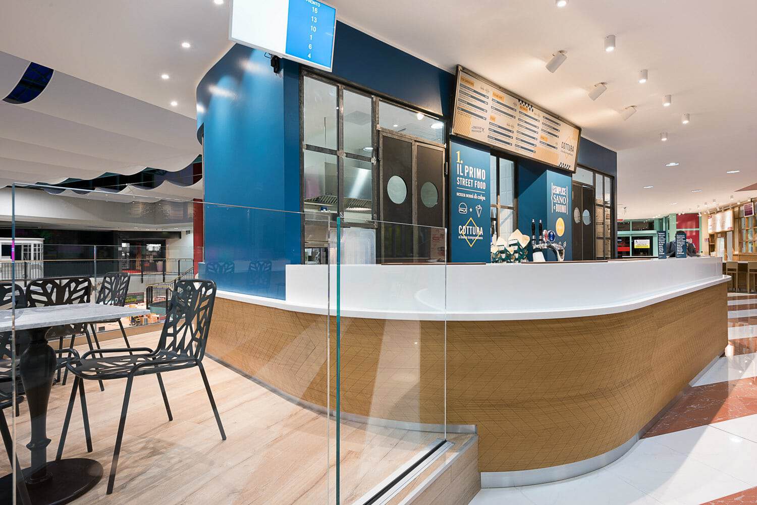 Modern cafe counter with blue accents and digital menu boards in shopping mall.