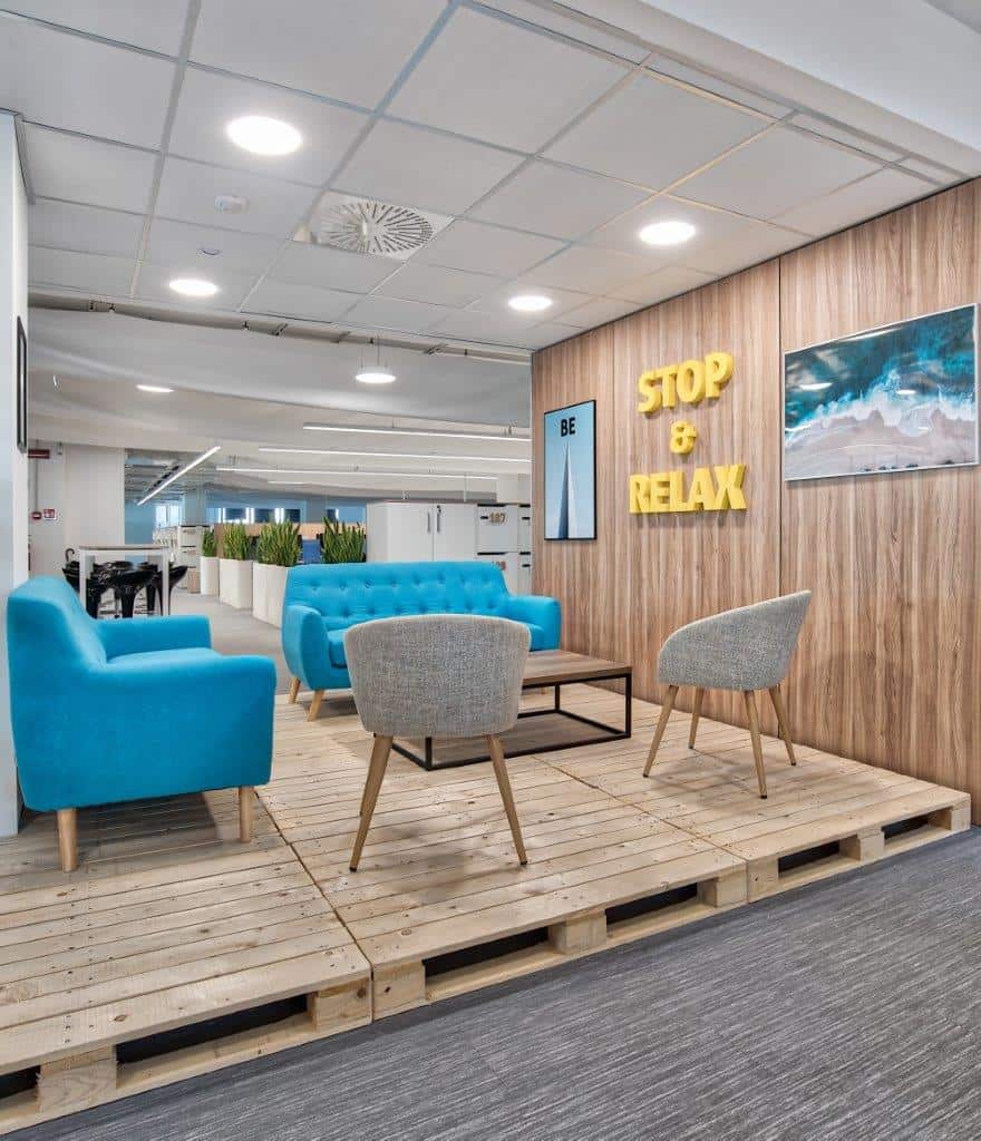 Modern office lounge with blue and gray seating and motivational wall decor.