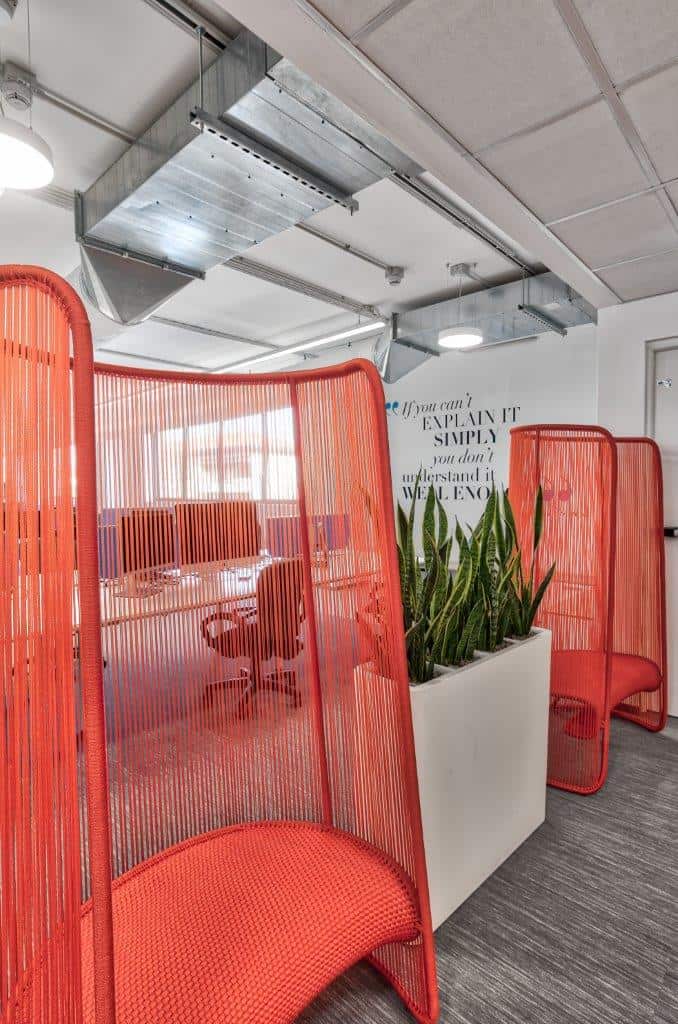 Modern office space with red privacy screens and green plants.