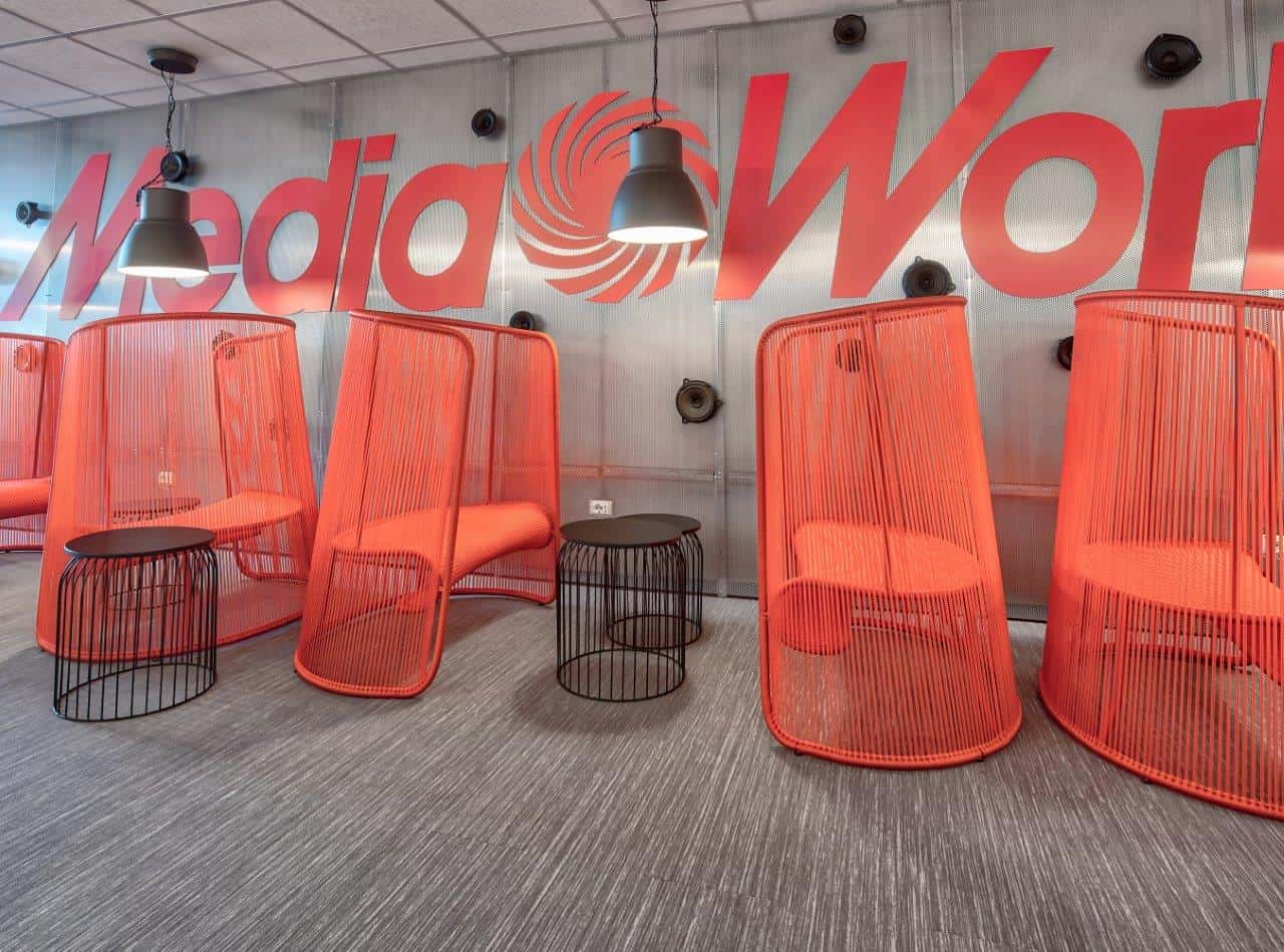 Modern office lounge with red pod chairs and media company logo.