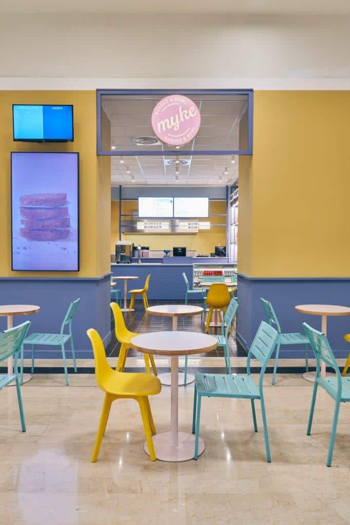 Modern interior of Myke Burger & Bowl Milan with colorful seating and digital menu screens.