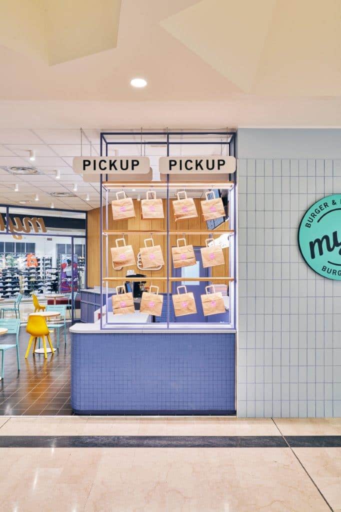 Order pickup counter at Myke Burger & Bowl Milan with display of bags and signs.