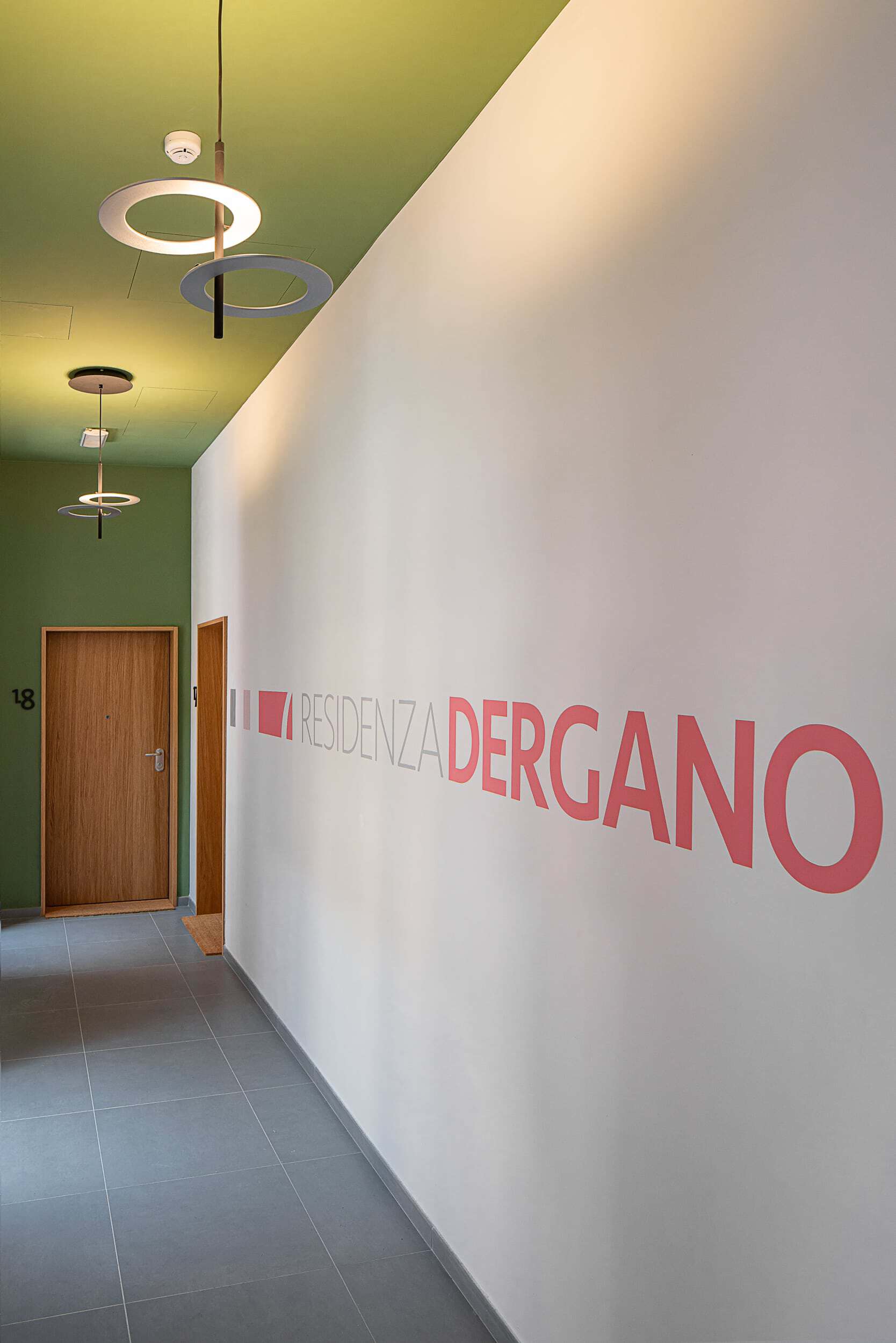Modern interior corridor with green ceiling and pink 'Residenza Dergano' sign.