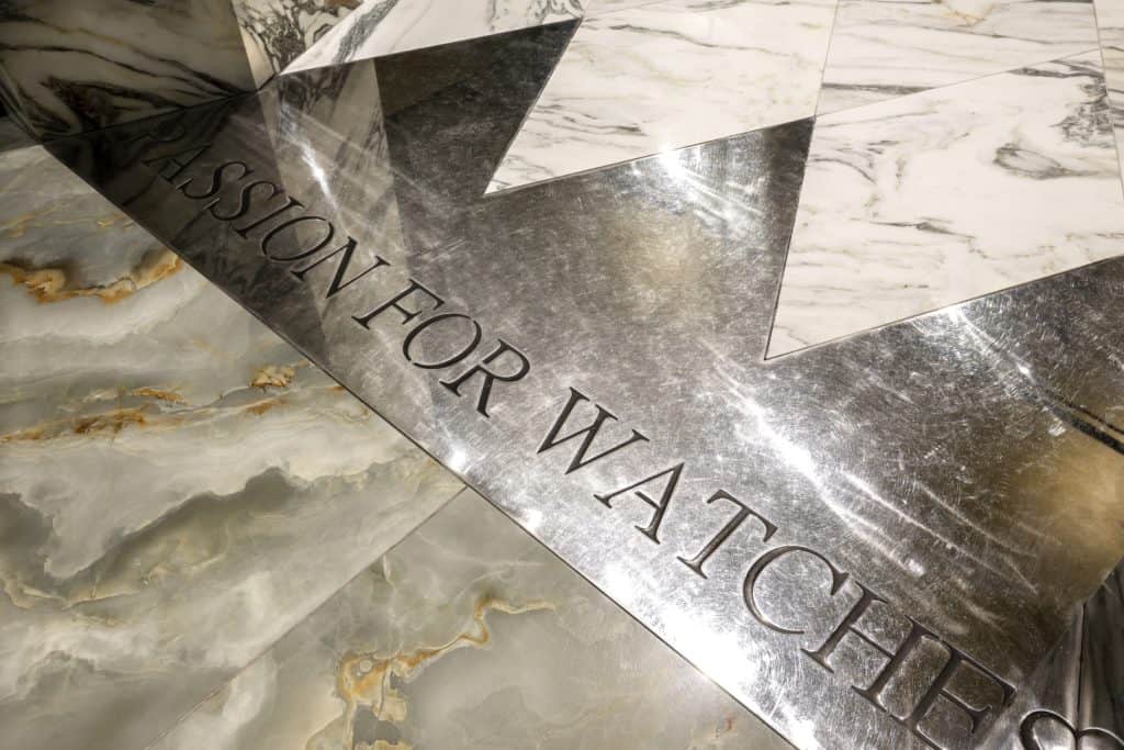 Marble Floor With Engraved Metal Plate Reading 'Passion For Watches'.