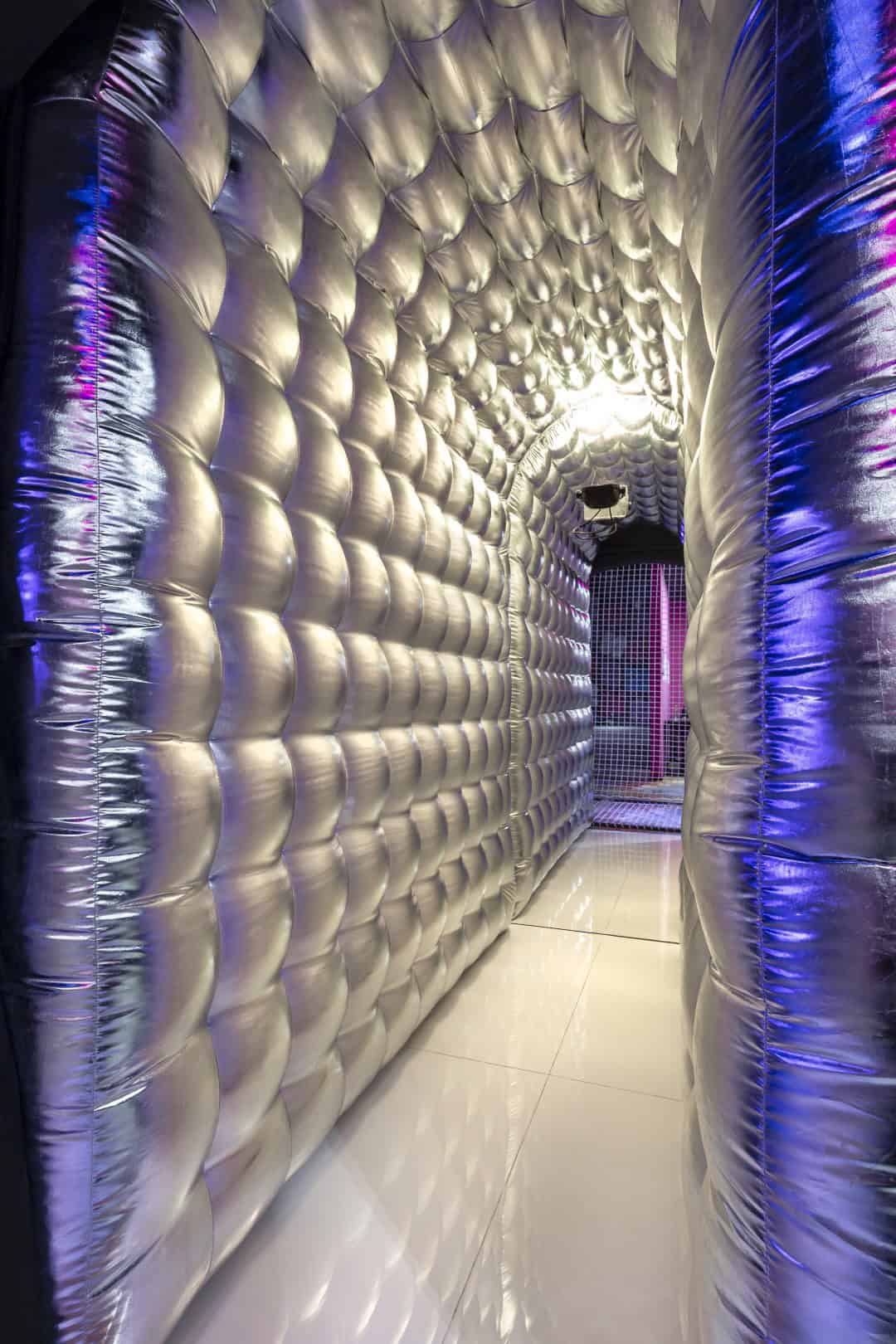 Futuristic metallic tunnel with quilted walls and colorful lighting effects.