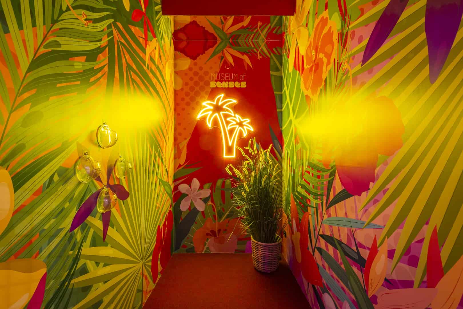 Vibrant tropical-themed corridor with colorful foliage and neon palm tree sign.