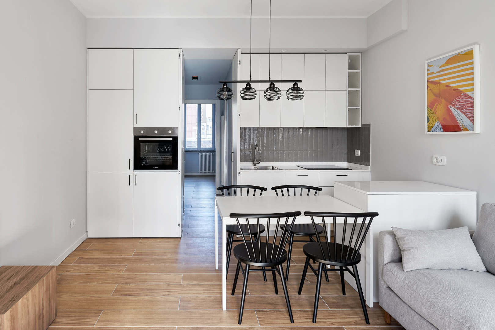 Modern white kitchen with dining area and wooden flooring.
